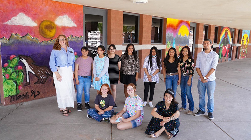 At left is Organ Mountains High School teacher Stefanie Japel. Standing at far right is Cruces Creatives community muralist Domenic Altamirano. In between, left to right, standing, are OMHS student muralists Jessica Arias, Reyna Arias, Gabriela Arias, Tahlor Triolo, Sarahi Alvarado, Jennifer Cordova and Mariana Cordova; and seated are student muralists Olive Japel, Mazie Japel and Cruces Creatives community muralist Celine Corral.