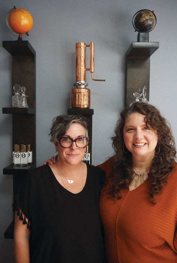 Laurajean Lewis and Erica Messenger stand under the smallest of the four copper stills that Lewis owns