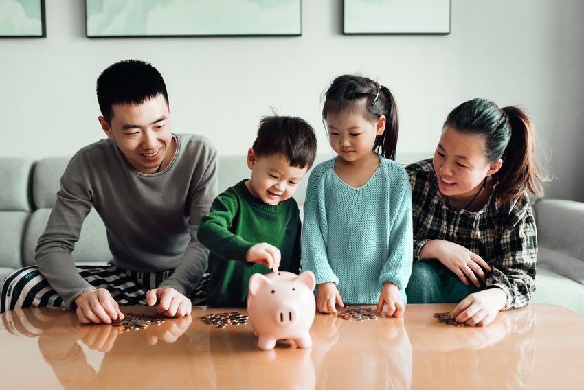 Young Asian family saving money together in a piggy bank