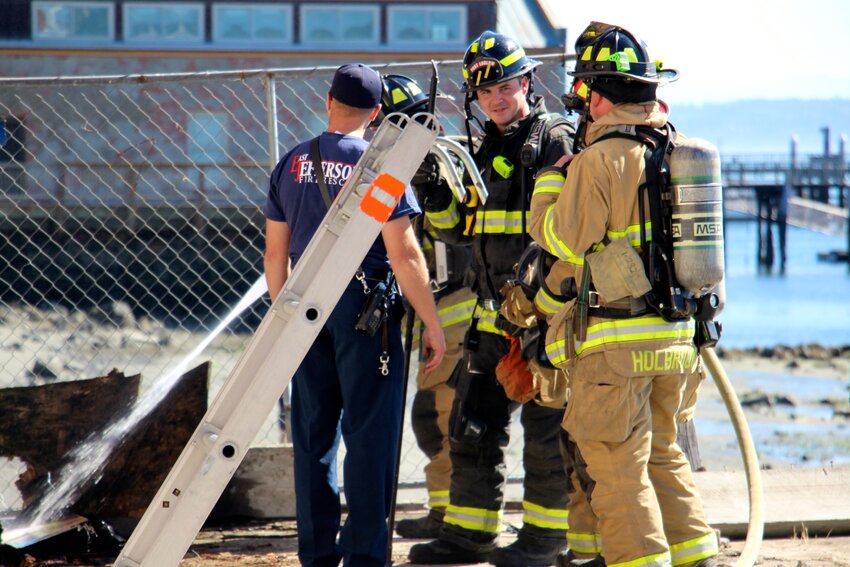 East Jefferson Fire Rescue Battalion Chief Jason MacDonald, in blue, consults with firefighters dousing a hot spot on the old Tyler Street wharf around 10:30 a.m. Friday morning.