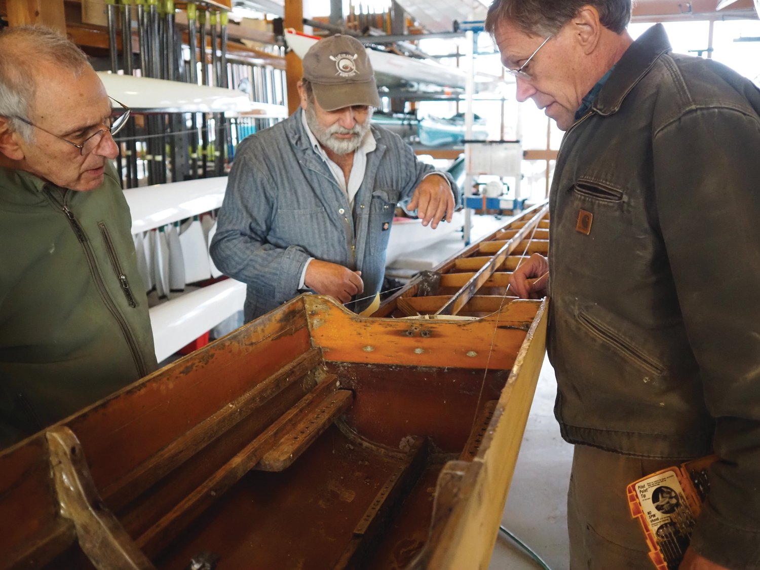 Paul Carter, right, discusses the delicacies of Dacron removal with members of the Rat Island Rowing Club. A leftover piece of the polyester fabric ironed on top of the rowing shell must be replaced without damaging the boat.