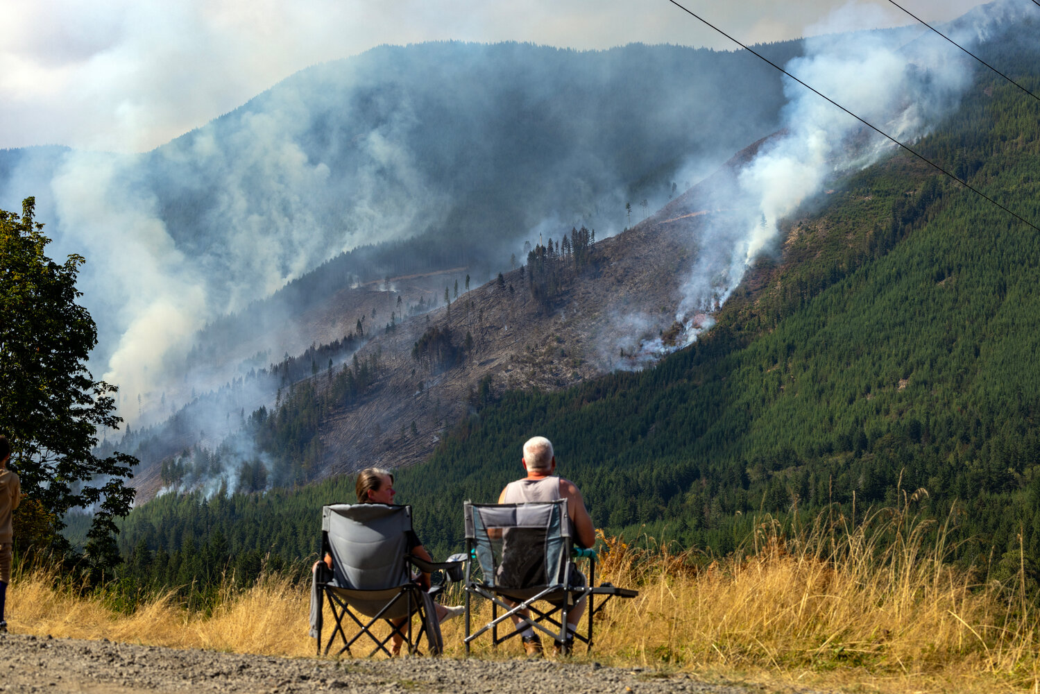 John and Christy Strickland sit in lawn chairs and watch as ground and airborne firefighters attempt to tame the wildfire on Mount Jupiter, west of Brinnon on Friday, August 17.