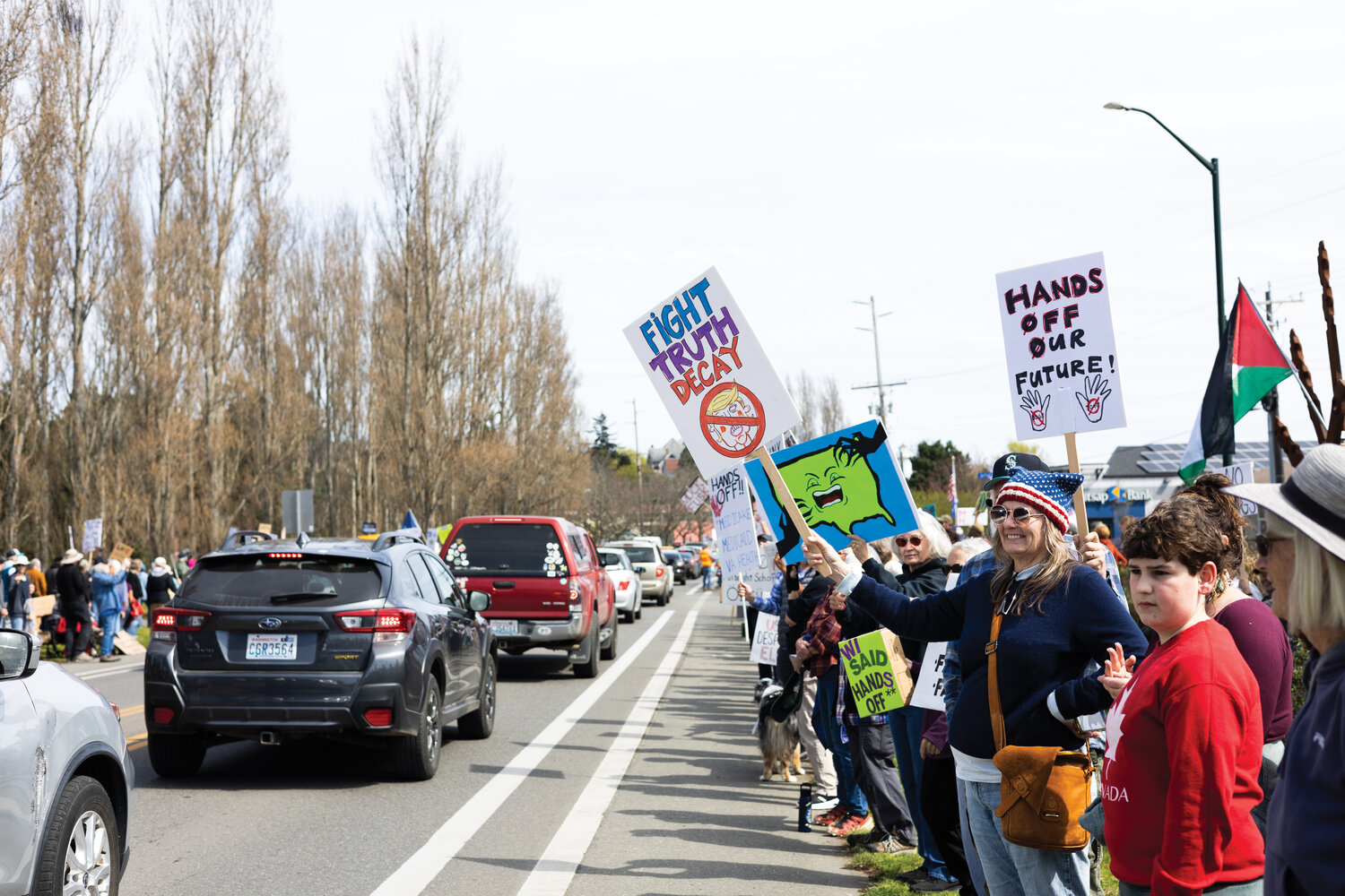 People waving signs in protest of the Trump administration line East Sims Way as cars pass on Saturday, April 5, in Port Townsend.