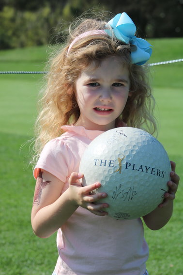 Avery Nilsson smiles big as she holds up a big souvenir golf ball she had signed by several players.