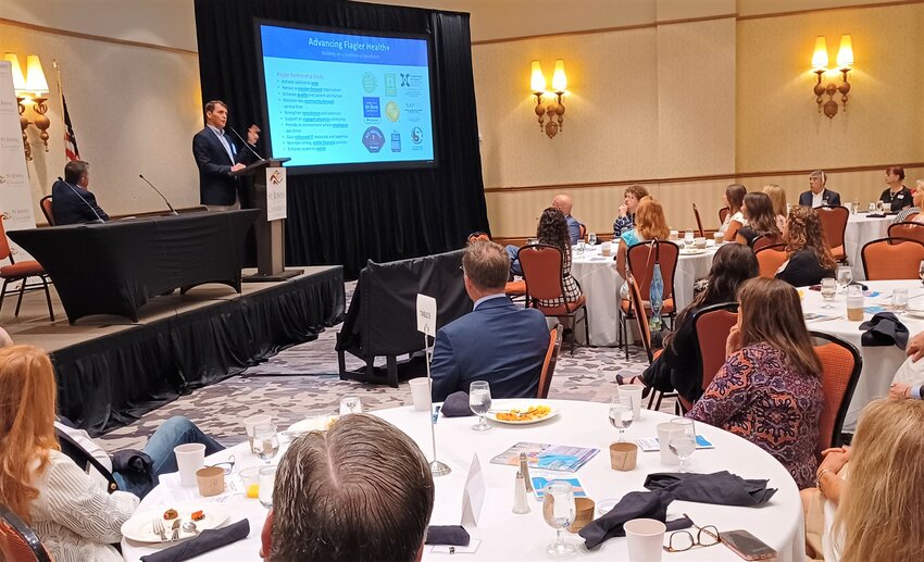Flagler Health+ President and CEO Carlton DeVooght addresses attendees at the recent St. Johns County Chamber of Commerce Economic Development Quarterly Breakfast as UF Health President David R. Nelson looks on.