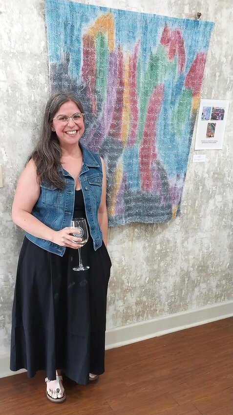 Textile artist Jessica Pinsky stands next to her recreation of her daughter’s painting. The work, “For Mira I,” is hand-painted cotton warp and assorted fibers.