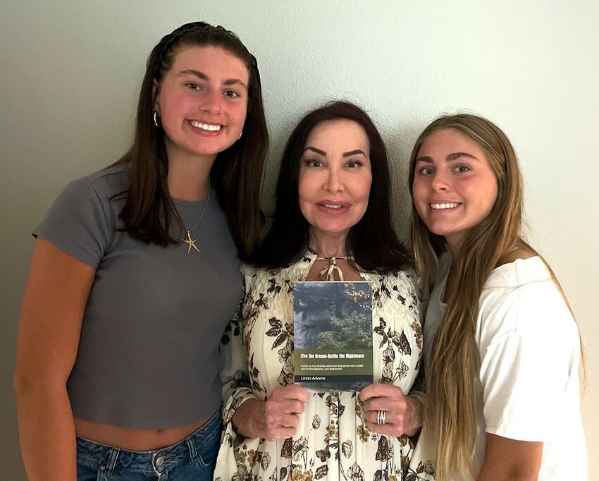Linda Adams holds a copy of her book with her stepdaughters Bella and Sophia Hayes by her side.