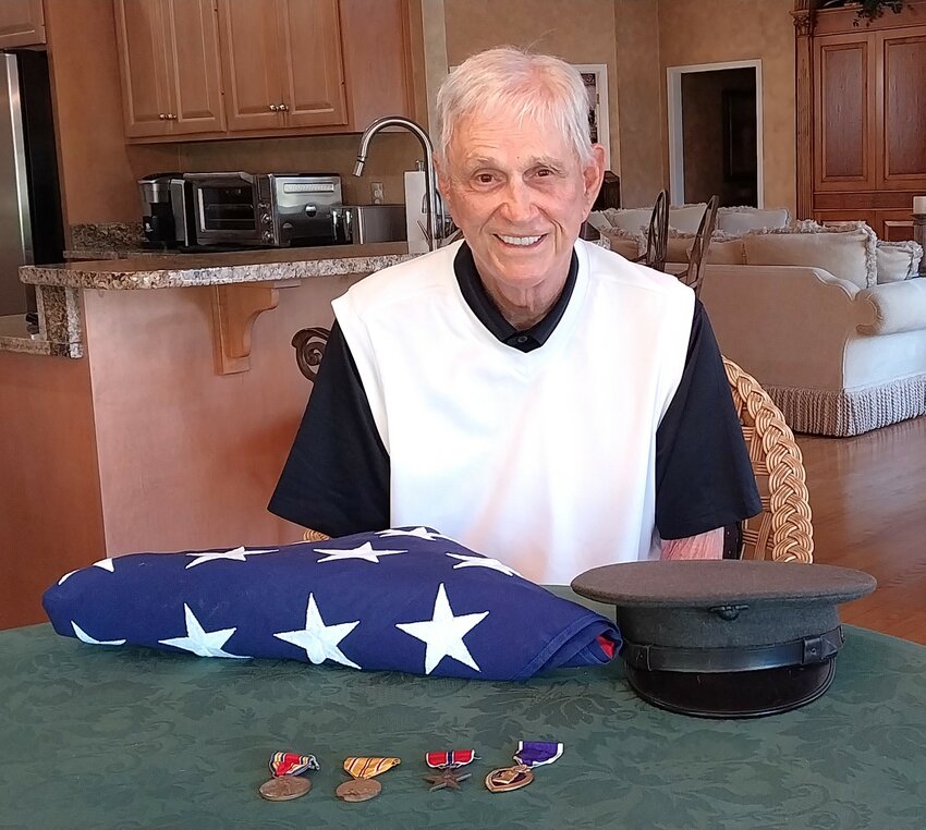 Hal Young sits at his dining room table with his father&rsquo;s flag, hat and medals.