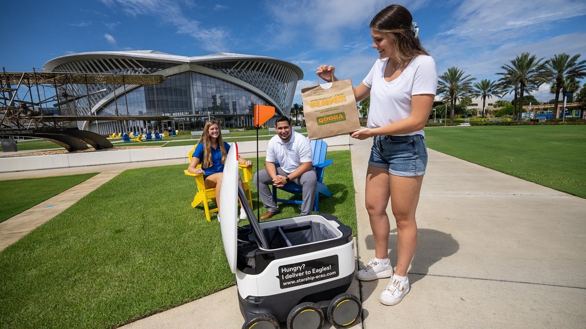 Students Hellie Jenkins, right, Johan Restrepo and Sydney Makarovich model the Sodexo Dining Services Starship Robots, at the Daytona Beach campus at Embry-Riddle Aeronautical University, Daytona Beach, FL, July 26, 2021. The robots will deliver all over campus autonomously