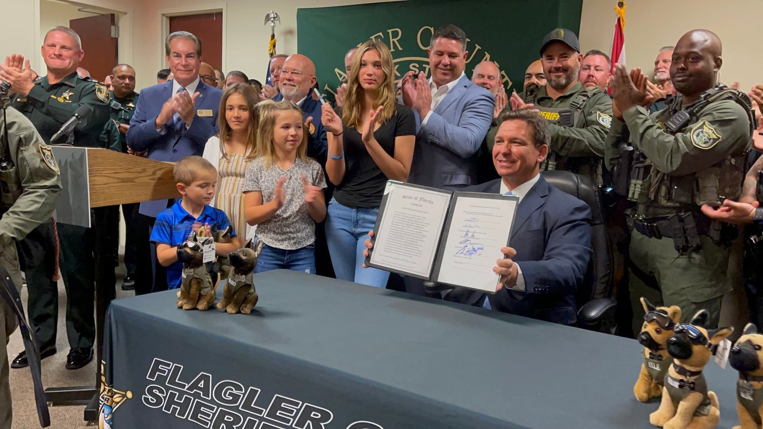 Emma Stanford, in black, stands next to State Senator Travis Hutson and Governor Ron DeSantis after the signing of the Care for Retired Police Dogs Program.