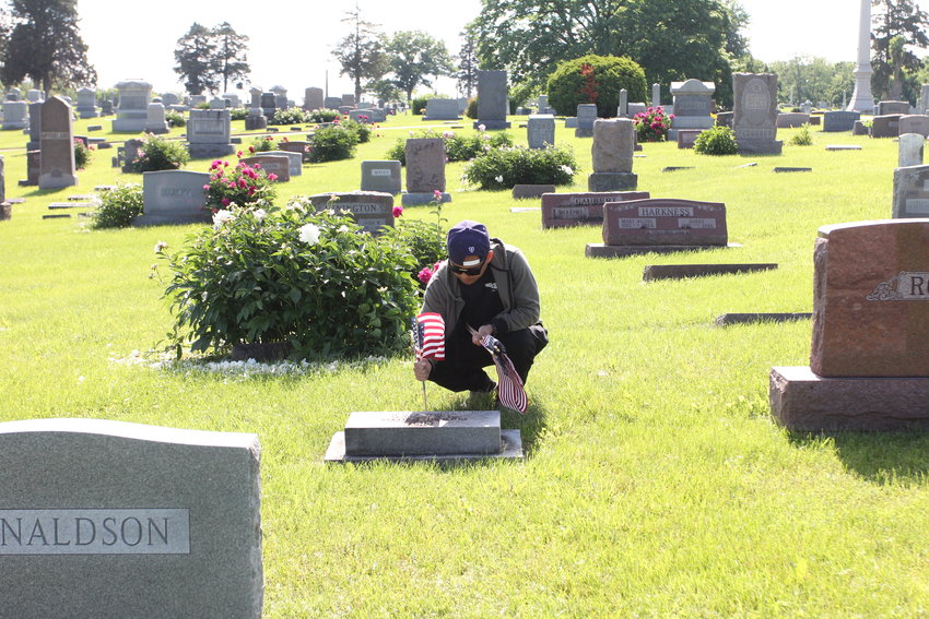 Fredy Yanos, U.S. Air Force, places a flag at a grave Friday, May 27, at Sunset Hill Cemetery.