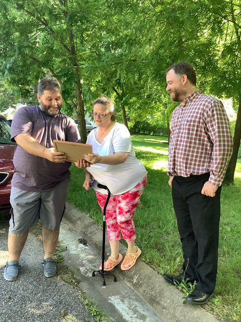 Fuller Center President Bryan Jacobs, left, and Vice President John Paul  Suchecki, right, present Dawn Collins with a framed photo of the Collins home on June 14 in Knob Noster in recognition of the family fulfilling its Greater Blessing obligation to the organization.