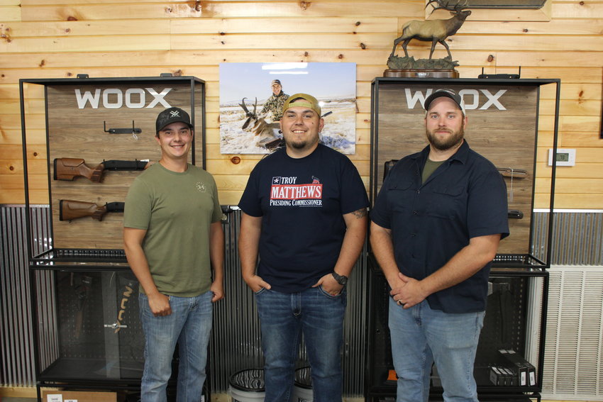 From left, Dylan Wickham, William Doak, and Adam Bell of Dogwood Outdoors pose in front of a hunting rifle case at Dogwood Outdoors. The sons of Doug Wickham and Billy Doak are following in their father&rsquo;s footsteps as they continue the family business.