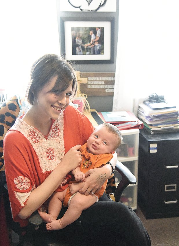 Kirstie Miller, of Sedalia, holds her son Leonides in her home office last week. She and her husband, Caleb Miller, own Thought Castles and create cups, mugs, jewelry, and other gift items.