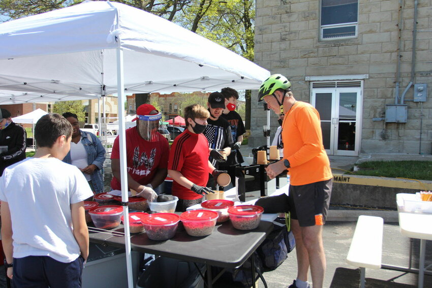 Jerome Coleman, in face shield, and employees of CG Foods make a batch of custom granola mix for Bruce Uhler during Opening Day for the 2022 season of the Warrensburg Farmers&rsquo; Market on Saturday, May 7, 2022, around the Johnson County Courthouse square. The 2023 season will begin May 6.   File photo by Sara Lawson | Star-Journal