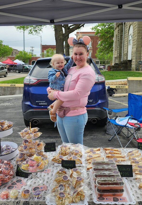Kelsey Gustin is pictured with her child in front of her booth at the Warrensburg Farmers' Market. Specializing in French- and Italian-style pastries, Gustin stays busy working to add new pastries to her booth.