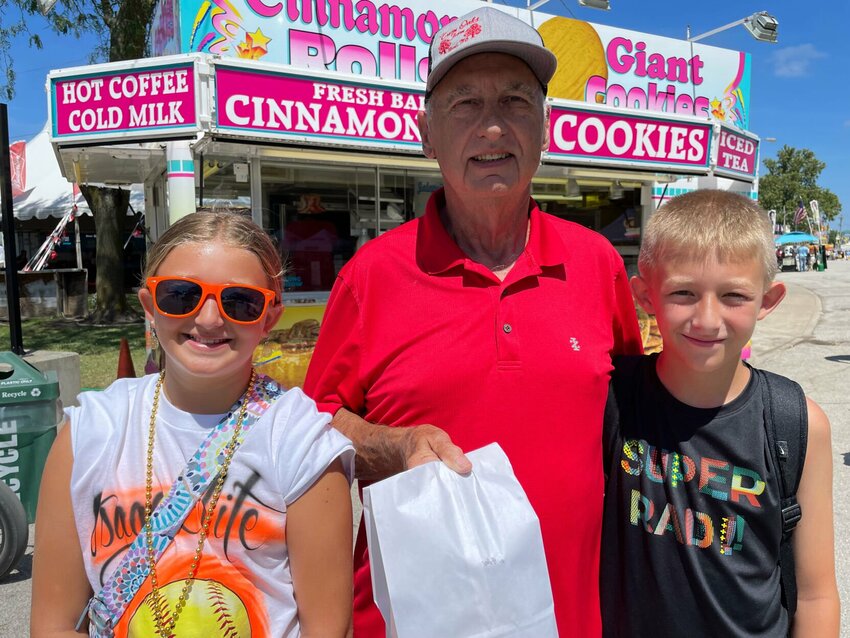 Michael Stockton has been visiting the cinnamon roll stand across from the arena at the Missouri State Fair each year for 55 years. Wednesday, Aug. 16, he treated grandkids Kennedy and Dakota to his fair food staple.   Photo by Chris Howell | Sedalia Democrat