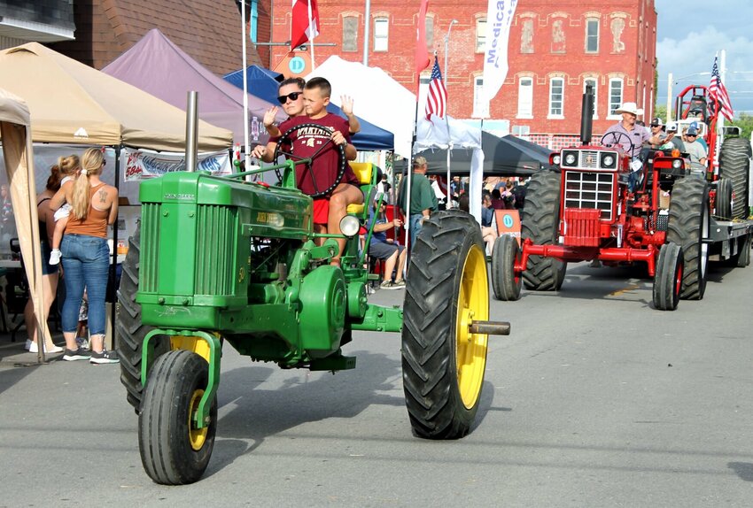 A young boy waves to the crowd lining the street in downtown Holden as he rides a tractor in the Holden Street Fair parade on Saturday evening, Aug. 26.