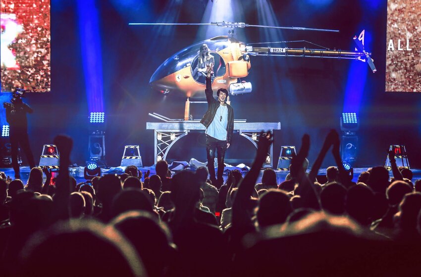 Reza stands with hand raised in front of a helicopter at a live show. Reza is bringing his illusion and magic show to Warrensburg on Oct. 5.