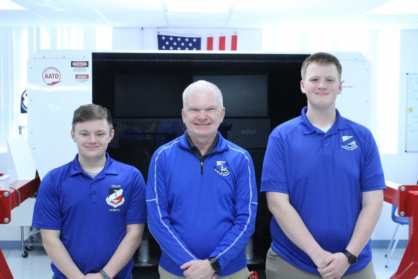 From left, Cadet Corps group commander Logan Hutchens, Senior Aerospace Science Instructor and coach Mark Talley, and CyberPatriot program coordinator Nathan Wiltrout pose for a photo in front of a flight simulator on Friday, Feb. 9, at Knob Noster High School. Photo by Zach Bott | Star-Journal