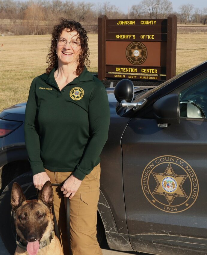 Wellness Coordinator Dawn Morris poses in front of the Johnson County Sheriff&rsquo;s Office sign with the department's K9, Ammo. Morris officially stepped into the role on Sept. 6, 2022, as the the county's first law enforcement wellness coordinator.