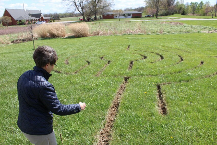 Teresa Pearce points to the entrance of the labyrinth on Thursday, April 11, at the Warrensburg Church of the Brethren.&nbsp;The path to the center is unobstructed, allowing the journey to be spiritual as you walk inside the labyrinth.&nbsp;