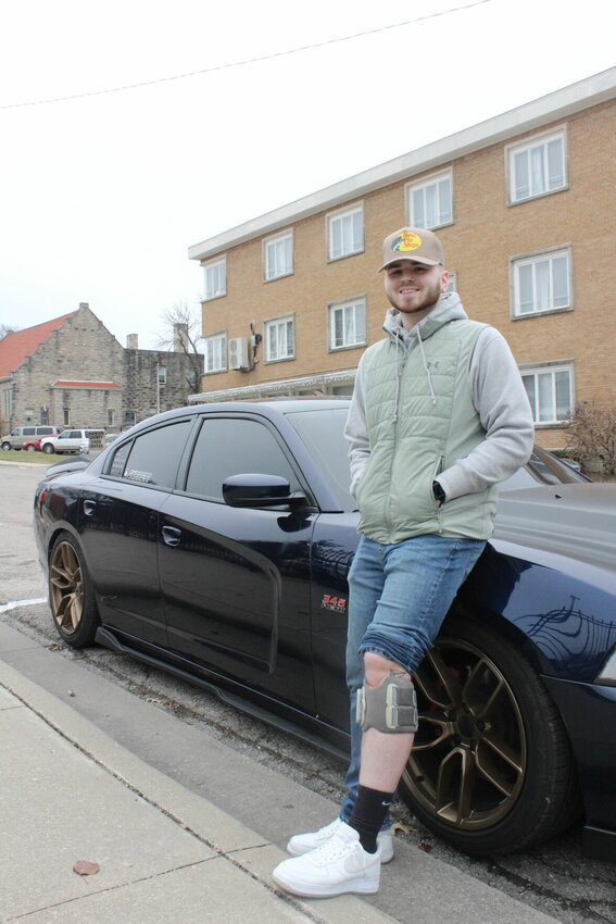 Garrett LaBelle, 25, leans on his car and shows off his Bioness L300 Go device on his left leg on Wednesday, Dec. 18, in Warrensburg. LaBelle was diagnosed with multiple sclerosis in 2021 at the age of 21 and was left bedbound for 18 months.&nbsp;