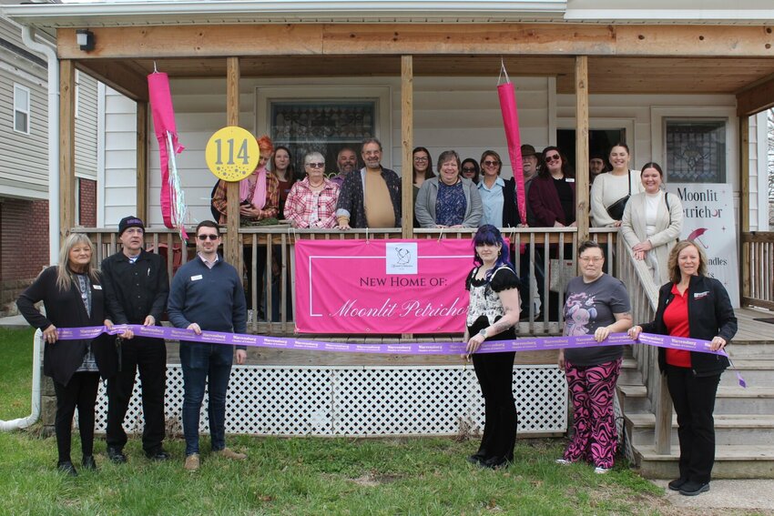 Warrensburg community members huddle together and pose for a photo during the ribbon cutting ceremony for Moonlit Petrichor's fifth anniversary and new location on Tuesday, April 1, at 114 W. Gay Street in Warrensburg.