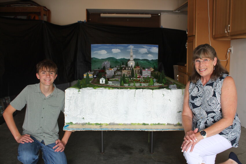 Jett Jewell, left, and his grandmother Roberta &ldquo;Bobbe&rdquo; Anson, right, pose for a photo in front of their model train set depicting the town of Colleville-sur-Mer, France, on Thursday, April 24, in Anson&rsquo;s garage in Warrensburg.