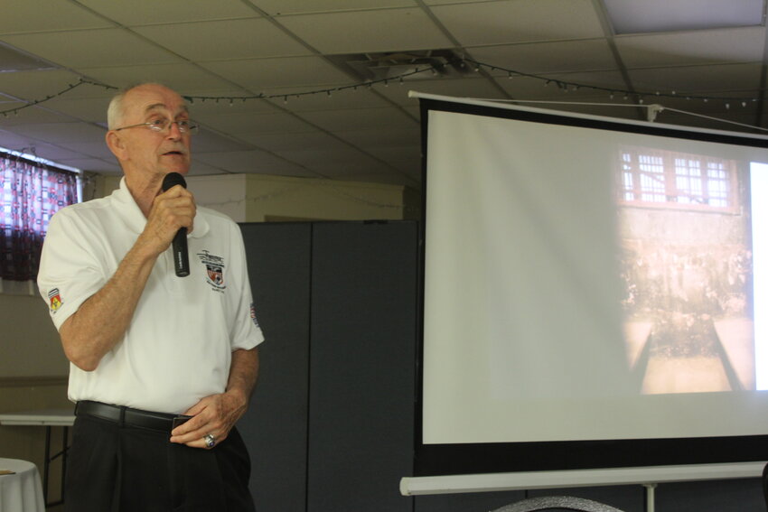: Ret. U.S. Air Force Major General Edward Mechenbier speaks in front of a photo of a prison cell on Wednesday, May 14, at the Matthews-Crawford American Legion Post 131. A Vietnam War POW, Mechenbier spent close to six years in the “Hanoi Hilton” prison.