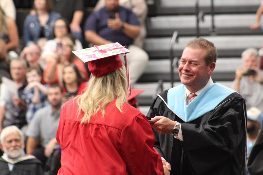 Warrensburg High School Principal Bret Pummill, right, smiles as he hands a diploma to a graduate on Saturday, May 17, at the Jerry M. Hughes Athletics Center. Saturday&rsquo;s ceremony was Pummill&rsquo;s last as the high school principal before retirement and he showed his emotions because of it.