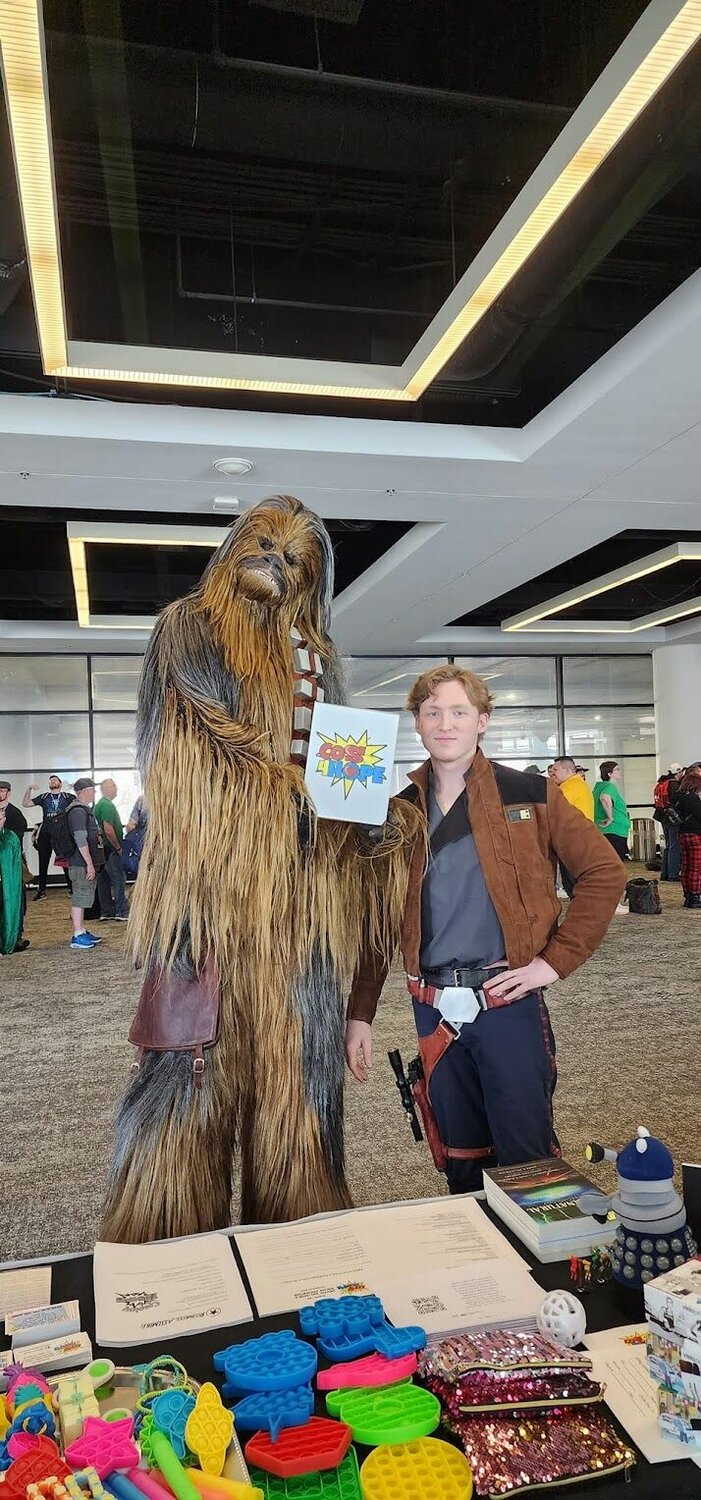 Participants cosplaying as Star Wars characters hold a Cos4Hope sign at a convention. 