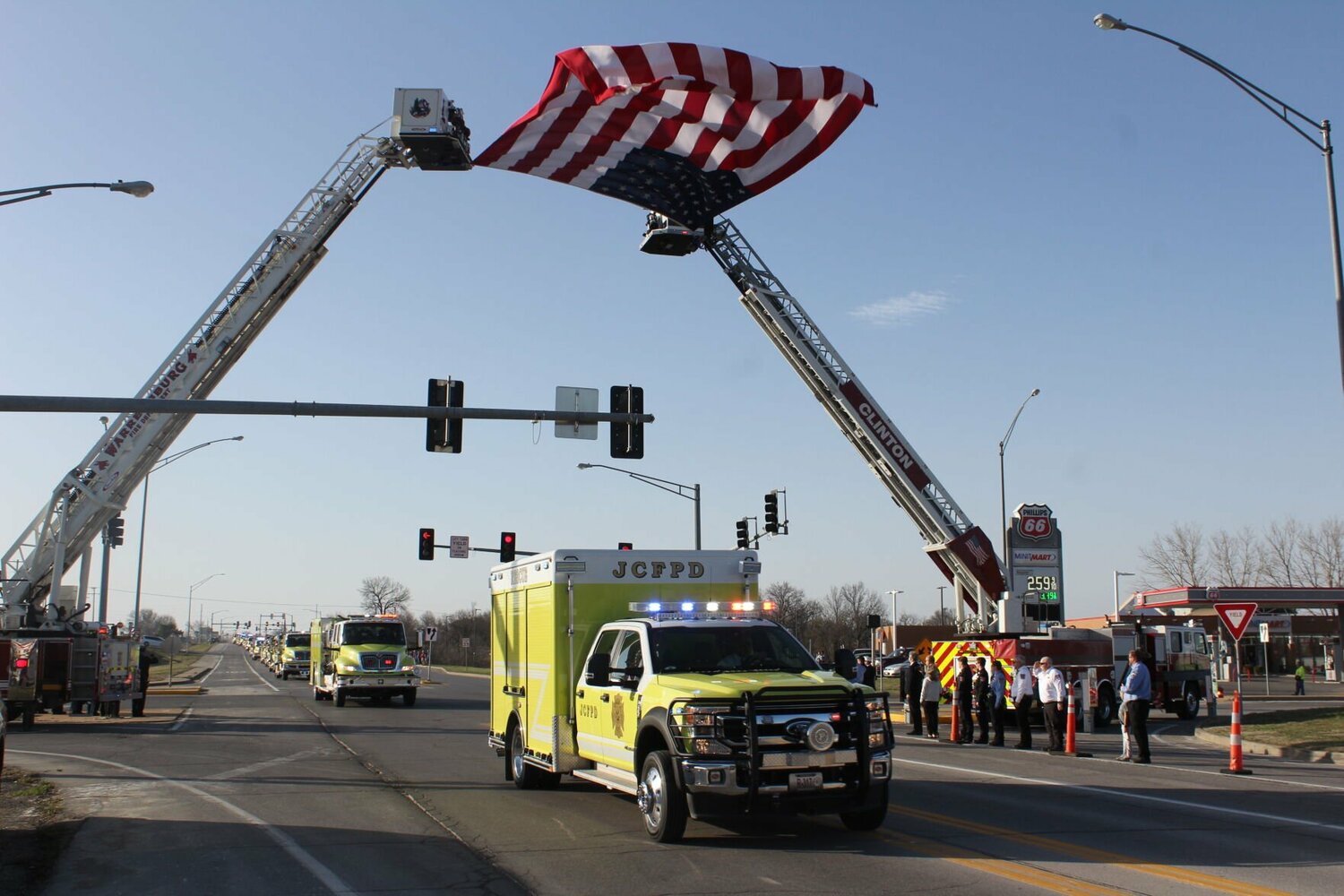 Johnson County Fire Protection District trucks drive under a flying American flag during the procession honoring fallen JCFPD Captain Vernon Collett on Friday, March 14, on Missouri 13 Highway in Warrensburg. Collett passed away on Saturday, March 8, after responding to a controlled burn.