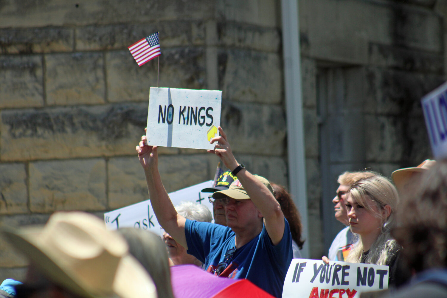 A protester holds a sign that states “no kings” with a United States floag attached Saturday, June 14, at the Johnson County Courthouse.