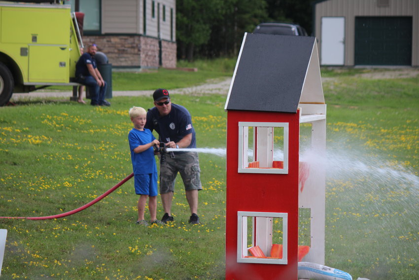 Cook Volunteer Firefighter Jon Rothluetner helps Grant Bixby Meehan, 8, hoist a hefty hose at the mock firehouse.