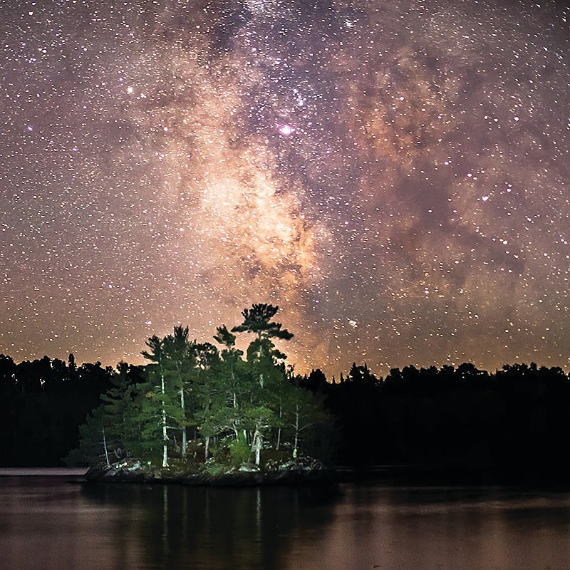 An island in   Voyageurs National Park, illuminated by flashlight with the Milky Way shining brightly above.
