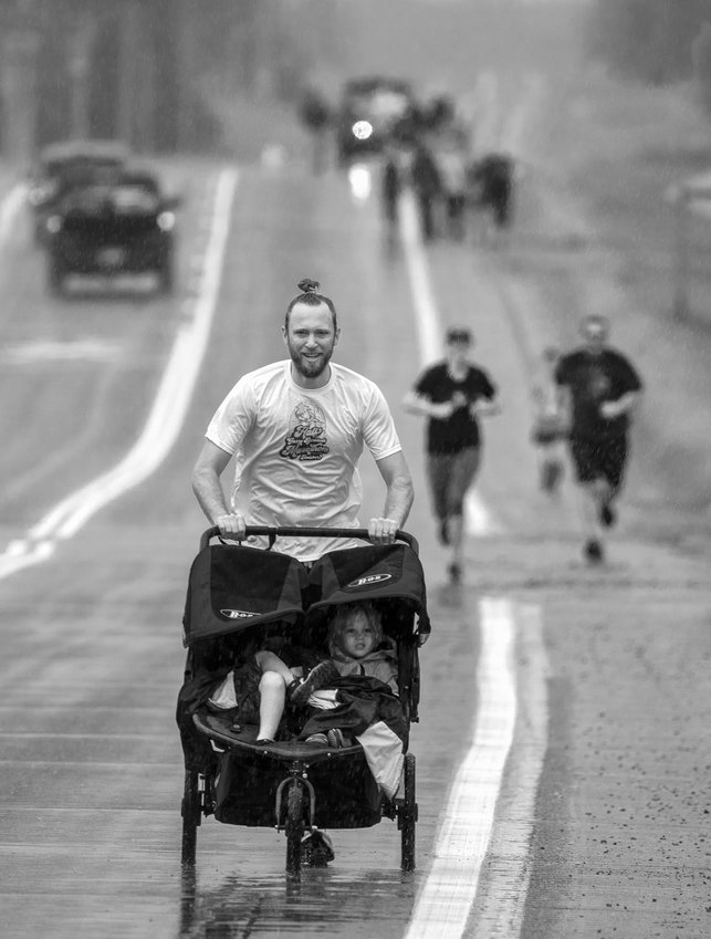 First place finisher Nathan Skon leads the pack down rain-spattered Ashawa Road while pushing his son Sebastian and nephew Anders.