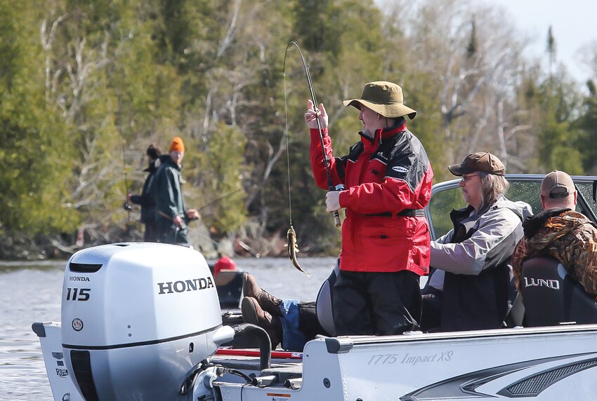 An opening day   fisherman lifts a little walleye into the boat while another nearby angler looks on.