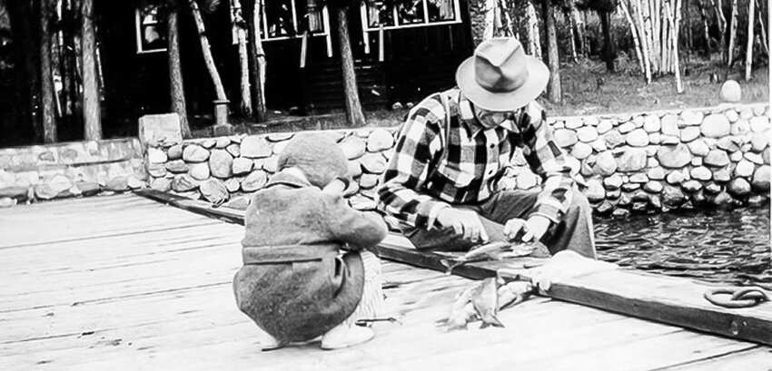 In an undated photograph, Martin Gundersen fillets fish on an area dock while one of his grandchildren watches with interest. Gundersen, along with his wife Elizabeth, were major property owners in the area in the early 1900s. They later donated much of that land to the city of Tower, some of which formed the basis for the Gundersen Trust.