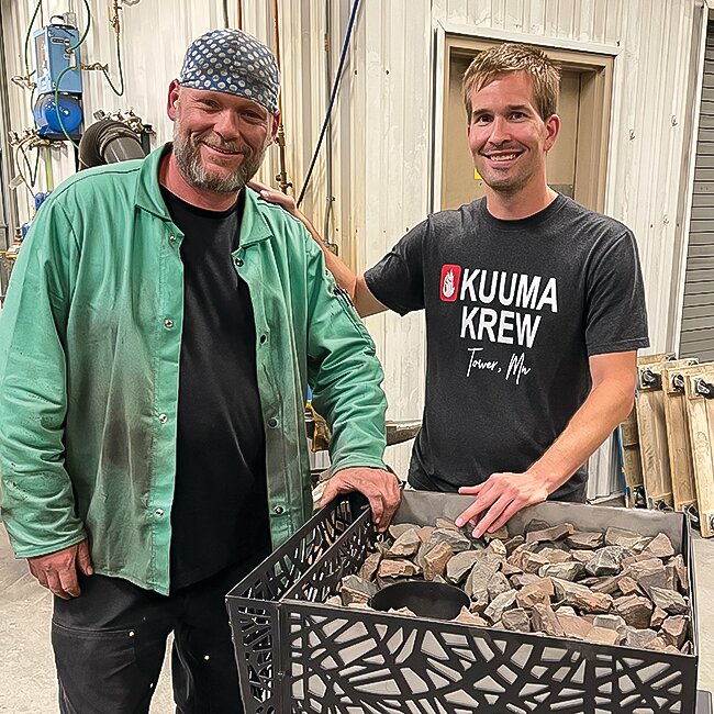 Garrett Lamppa (r) and Todd Petersen stand along a version of the new wood gasification sauna stove Lamppa Manufacturing is preparing to launch soon.