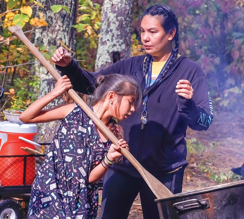 Jennalee Porter watches over Lauren Miigizikwe Bajan as she practices stirring wild rice in a   parching pot.