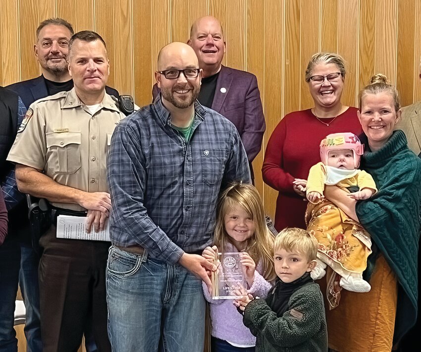 Joe Froehlingsdorf helps his children Agnes and Joey hold his 911 Lifesaver Award as his wife Ida holds their daughter Amelia. Presenting the award was Sheriff Gordon Ramsay, left, with commissioners Mike Jugovich, Paul McDonald, and Annie Harala looking on.