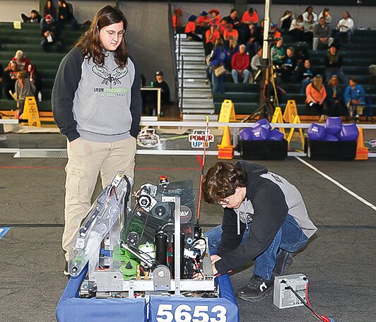 Greyson Reichensperger kneels down to replace a dead battery on the team&rsquo;s robot while teammate Ian Sunsdahl assists.