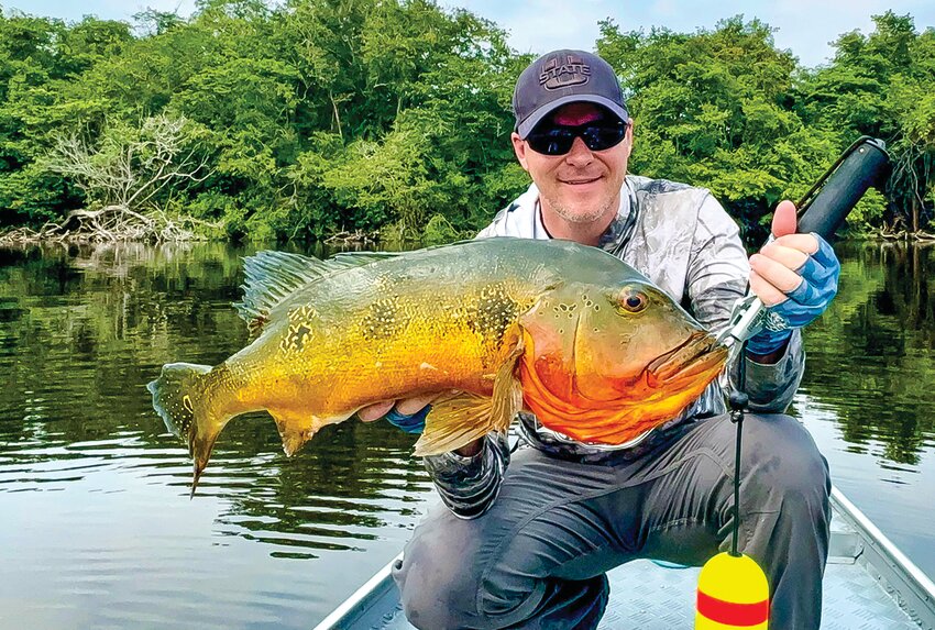 Adam Van Tassell poses with his world record-sized fire peacock bass on a boat in the Amazon