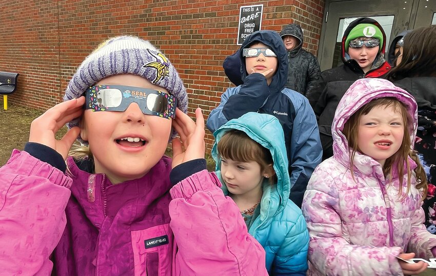 Ayva Anderson and classmates stand in the drizzle with their eclipse glasses