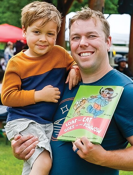 Author Nicholas DeShaw holds his son Magnus with one hand and his new children&rsquo;s book about   powwows at the SahGiiBahGah powwow at Nett Lake earlier this month.