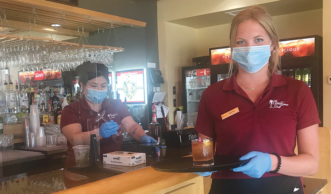Bartender Joett Baldwin, left, and server Kaylee Iverson wear protective face masks and gloves while serving guests at the Wilderness Grill at Fortune Bay Resort Casino.