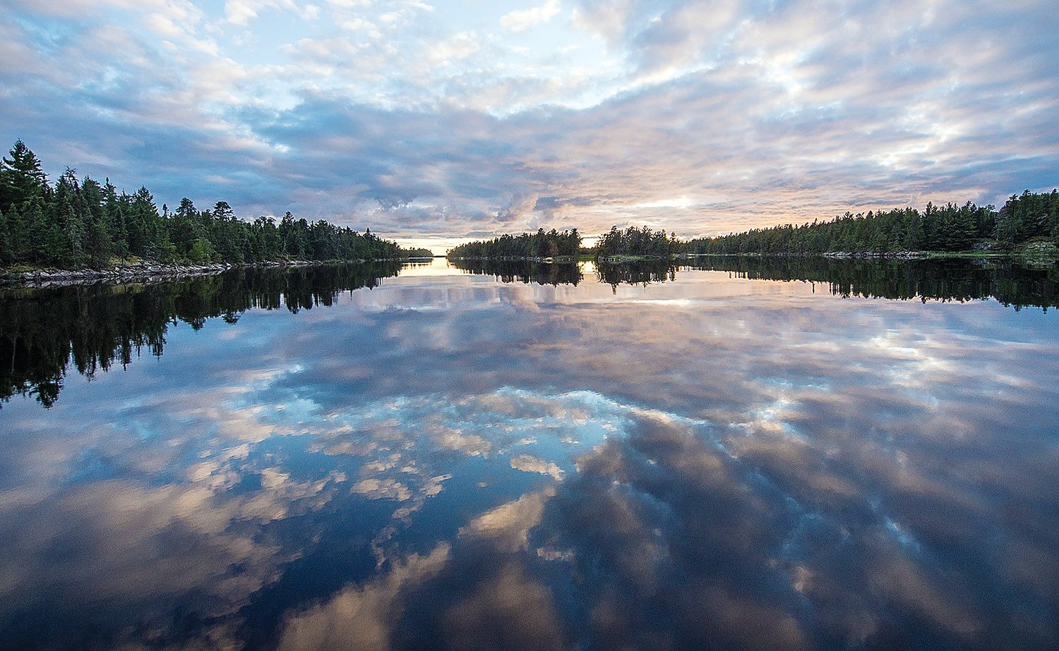 Clouds at sunset reflect in the calm waters of the Rainy River. The river has made an extraordinay comeback in terms of water quality since the introduction of environmental regulations in the 1970s.