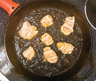 Bacon-wrapped Hawaiian chicken rumaki sizzles in a pan of oil.