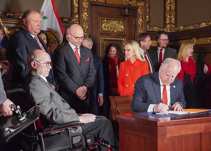 Sen. David Tomassoni, seated left, watches as Gov. Tim Walz signs the bill providing $25 million for ALS research and caregiver support.